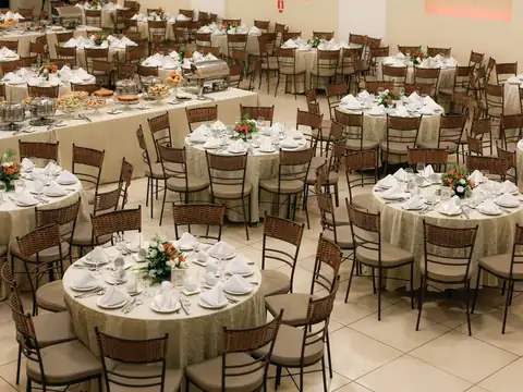 A banquet hall seen from above, with round tables set with plates, napkins and flowers, and a buffet table along one side
