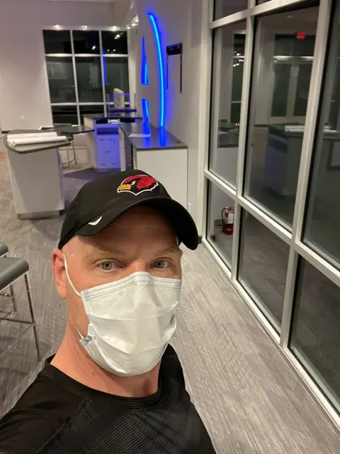 The owner's selfie in a black cap and a face mask inside a showroom at night