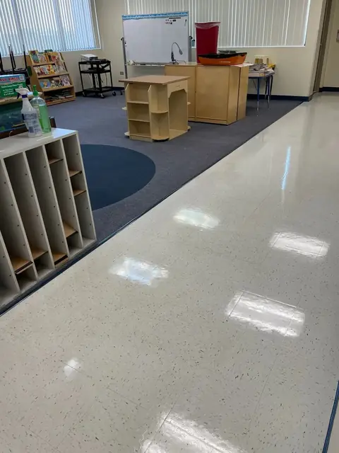 A classroom tile floor shining under the ceiling lights, beside a row of cubbies and a blue carpet