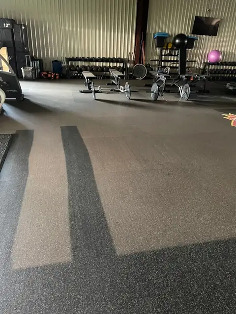 A gym's rubber floor covered in pale dust, with two dark stripes of clean floor running through it, and weights and benches behind