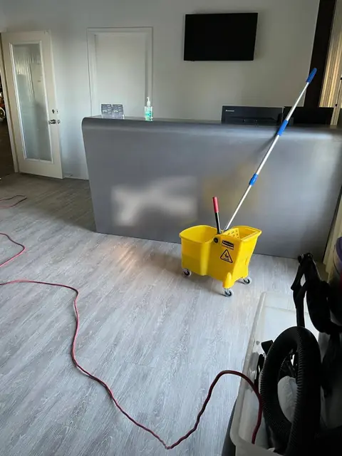A gray front desk on a wood-look floor, with a flat mop leaning against it, a yellow mop bucket in front and an extension cord across the floor