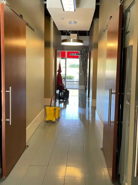 A hallway with wooden sliding doors on both sides and a glossy tile floor, with a yellow mop bucket at the far end