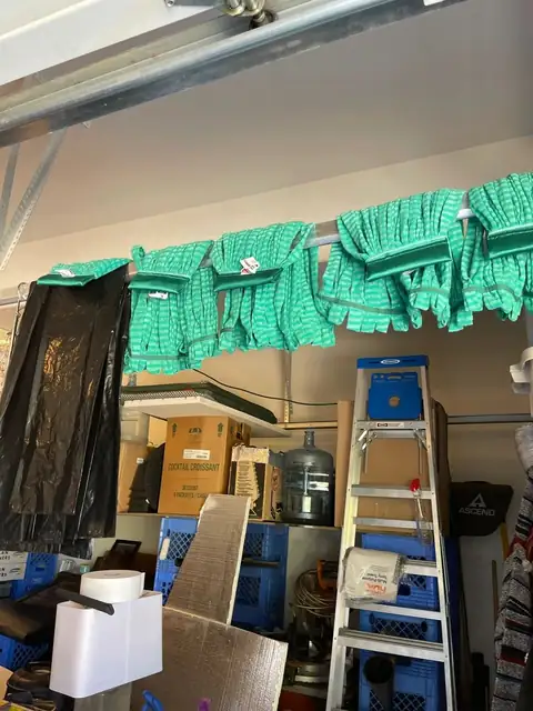 Green mop heads and black trash liners hung over a rail in a storage space, above shelves and a step ladder